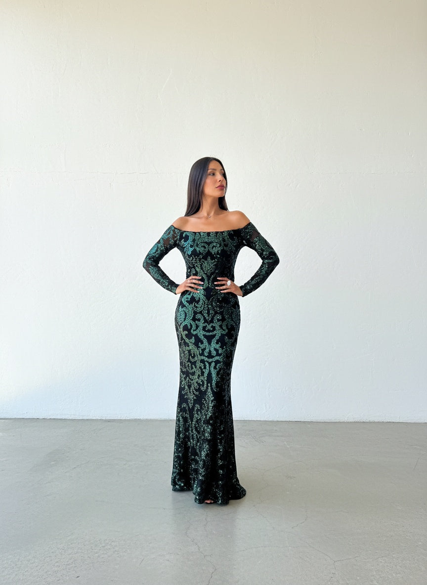 Vestido de lentejuelas verde botella sobre fondo negro, con escote strapless y mangas largas ajustadas.