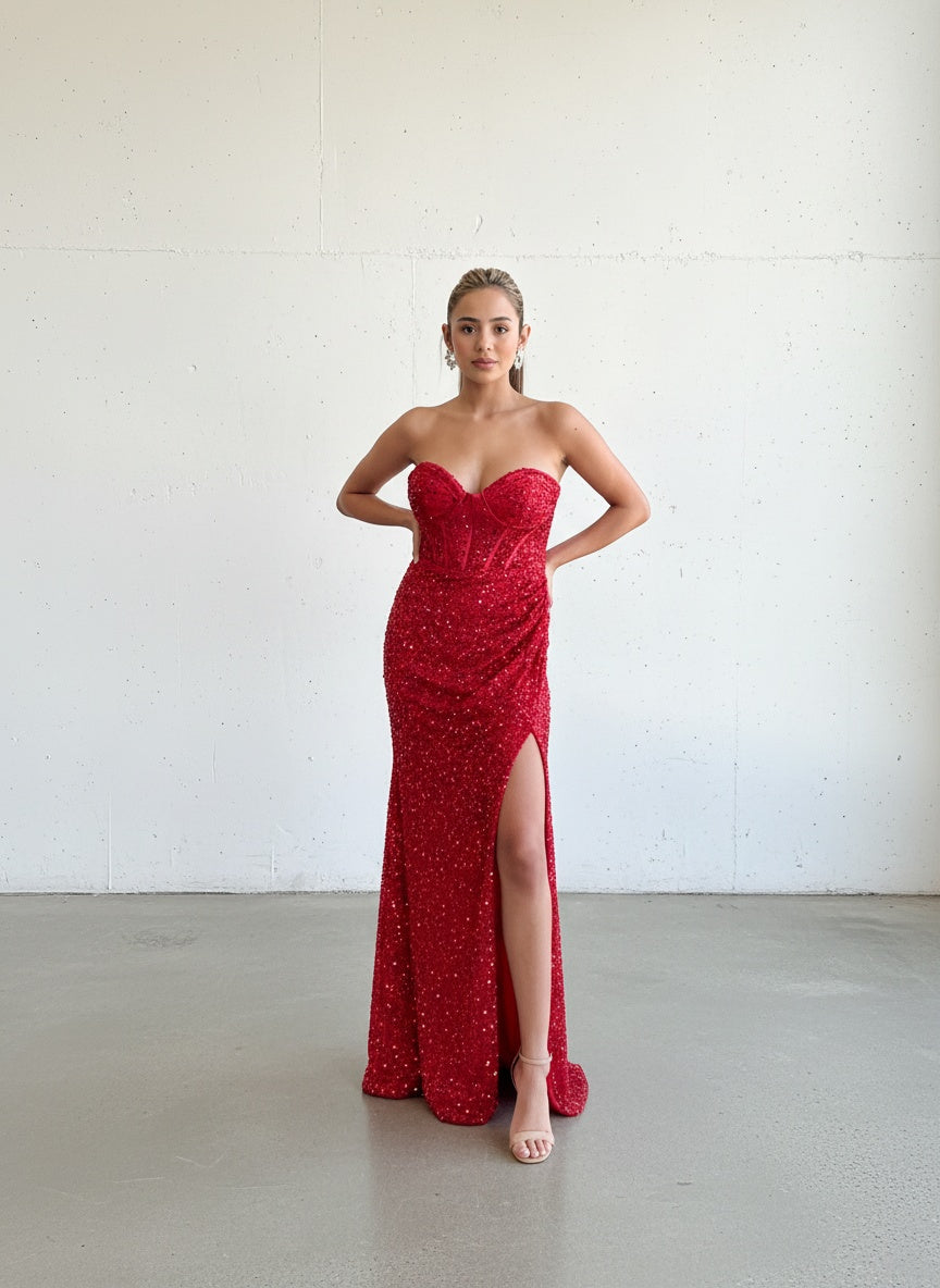 Modelo con vestido largo rojo de lentejuelas, escote strapless tipo corset y tajo lateral pronunciado