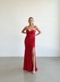 Modelo con vestido largo rojo de lentejuelas, escote strapless tipo corset y tajo lateral pronunciado