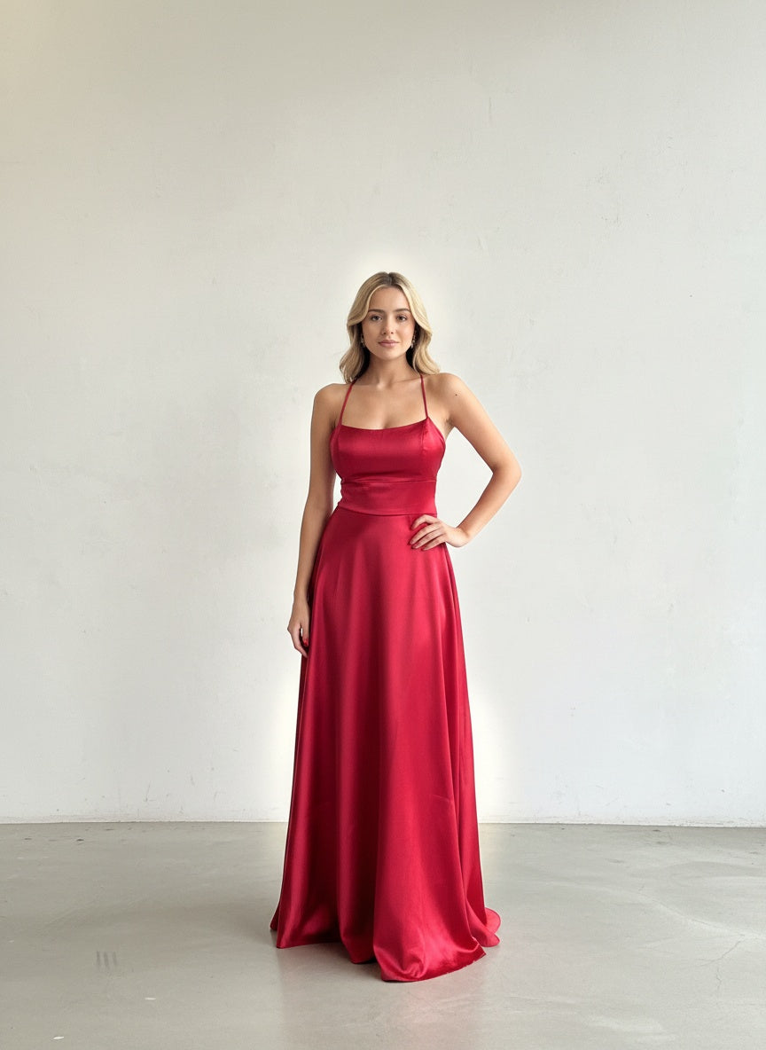 Modelo con vestido largo de satín rojo vibrante, con escote recto, tirantes delgados y falda con bolsillos