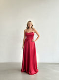 Modelo con vestido largo de satín rojo vibrante, con escote recto, tirantes delgados y falda con bolsillos