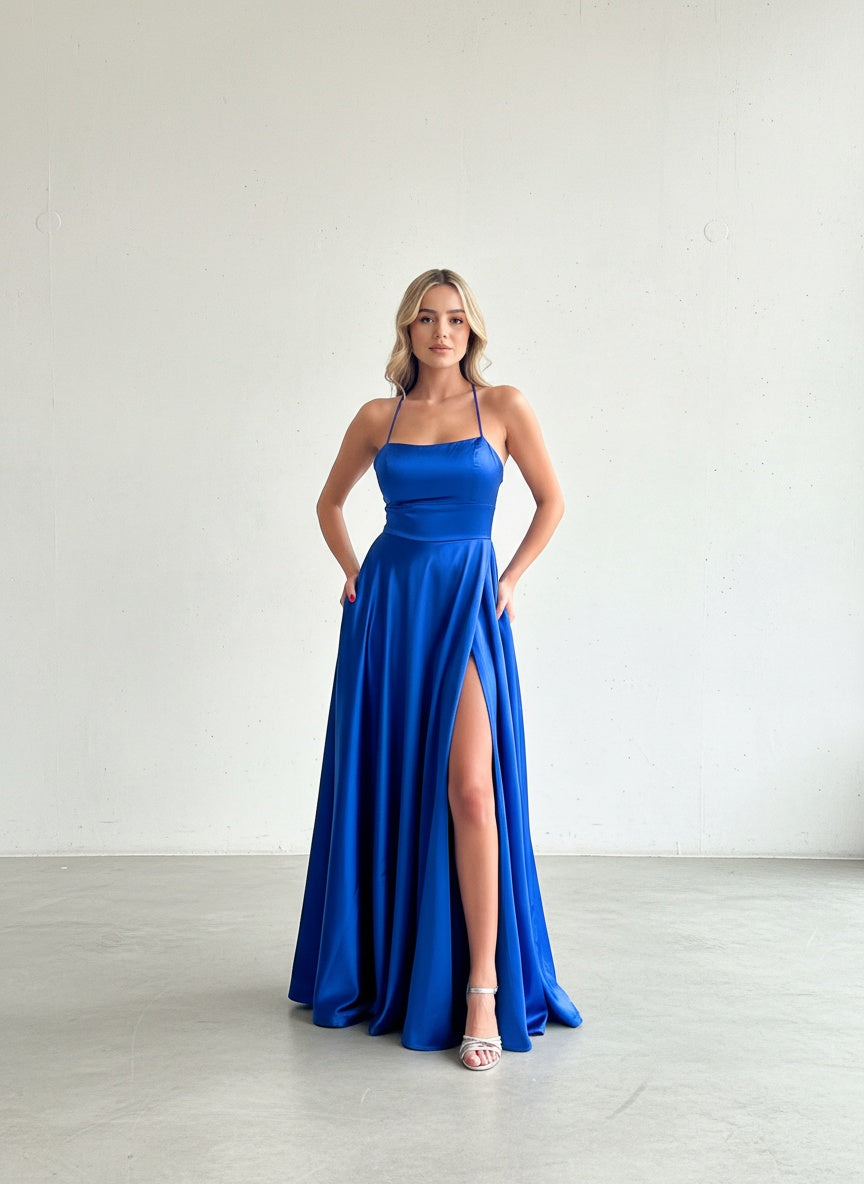 Modelo con vestido largo de fiesta azul rey en satín, con escote en V, tirantes delgados y falda fluida con bolsillos