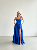 Modelo con vestido largo de fiesta azul rey en satín, con escote en V, tirantes delgados y falda fluida con bolsillos