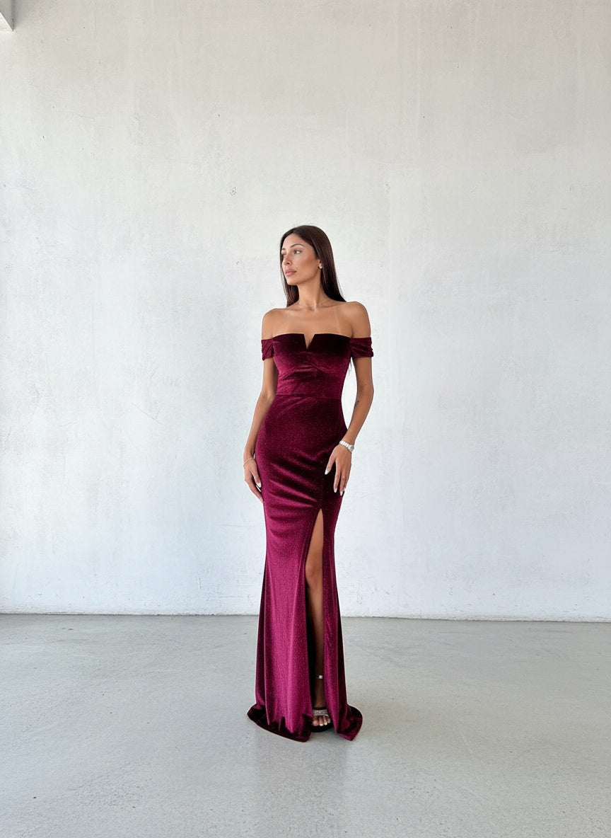 Modelo con vestido largo de terciopelo burdeo con brillos, escote bote y tajo lateral pronunciado