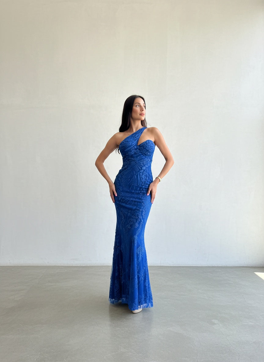 Modelo con vestido largo asimétrico de un hombro, con aplicaciones de mostacillas brillantes en el torso y tajo lateral en la falda